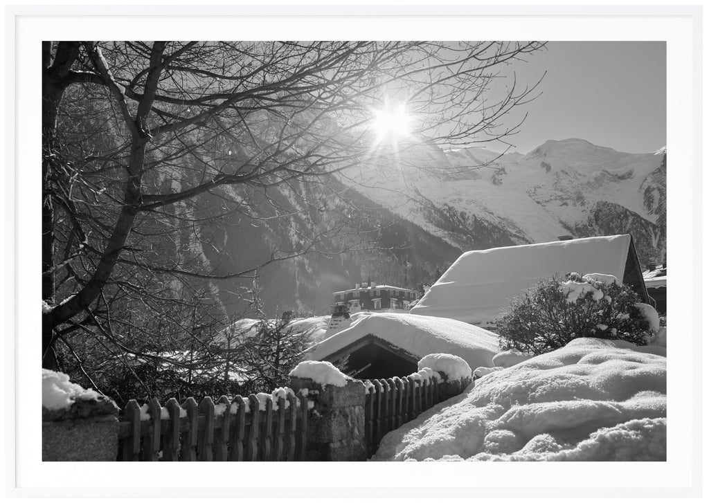 Black and white photograph of snow-covered rooftops with alps in the background. White frame.