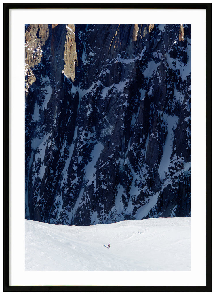 Color photograph of lone mountaineer with steep cliffs in the background. Black frame. 