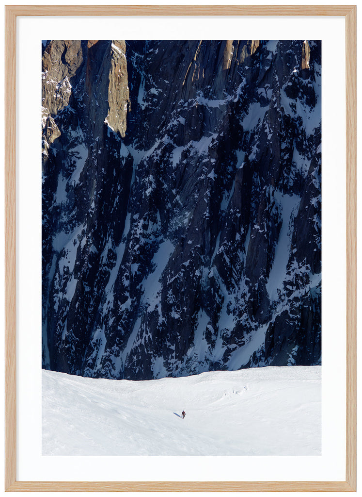 Color photograph of lone mountaineer with steep cliffs in the background. Oak frame.