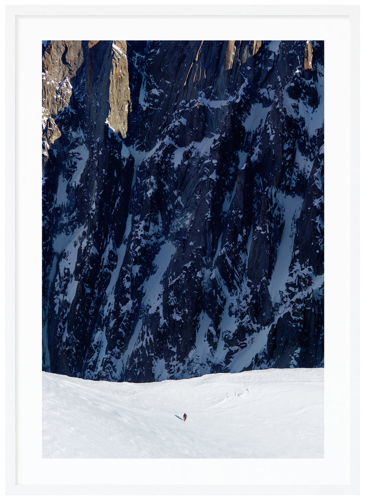 Color photograph of lone mountaineer with steep cliffs in the background. White frame.