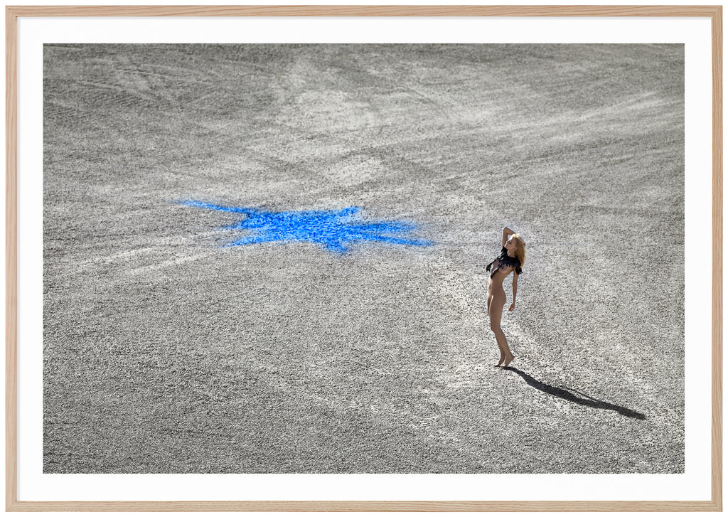 Color photography in landscape format of a naked woman standing on stone ground with a blue figure on. Oak frame. 