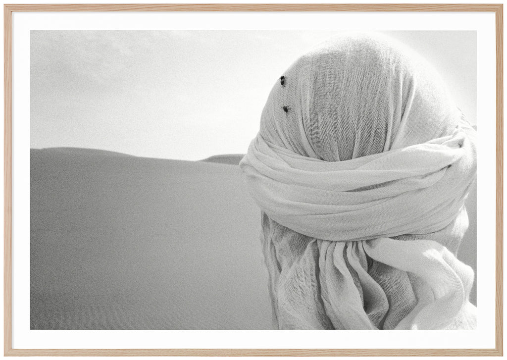 Black and white poster of close-up on head from behind with white shawl and two flies on in the desert. Oak frame.