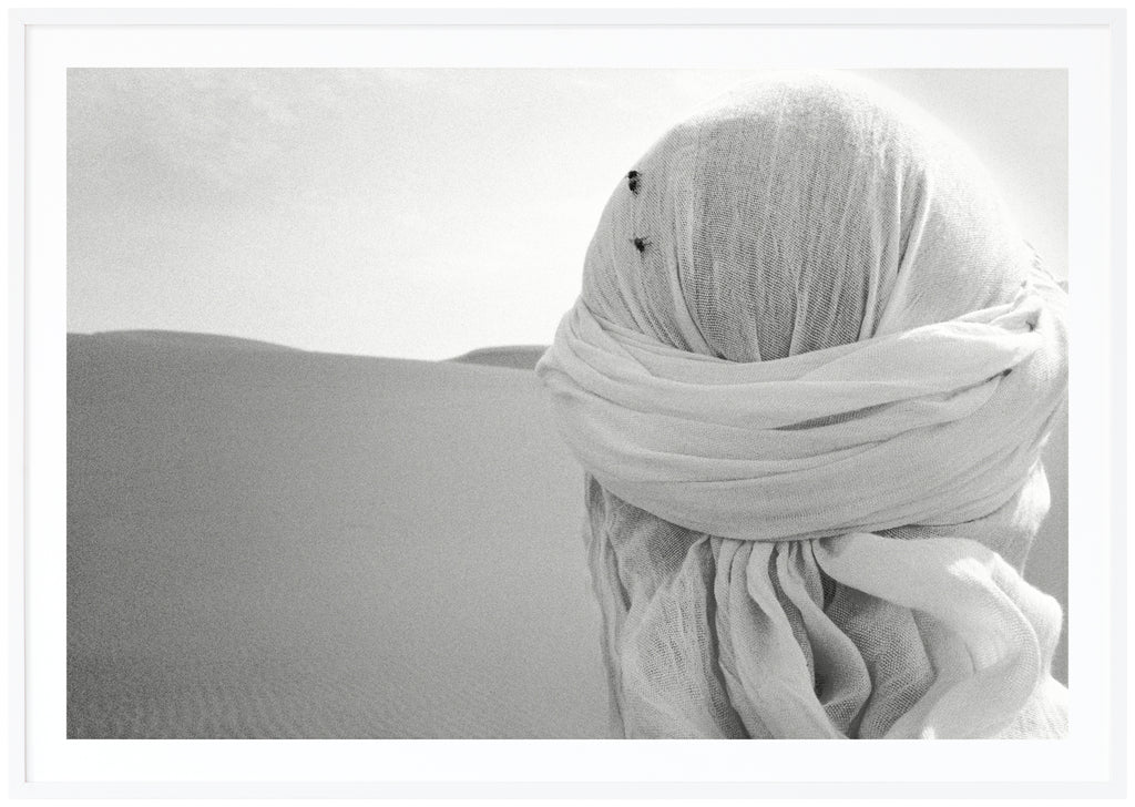 Black and white poster of close-up on head from behind with white shawl and two flies on in the desert. White frame. 