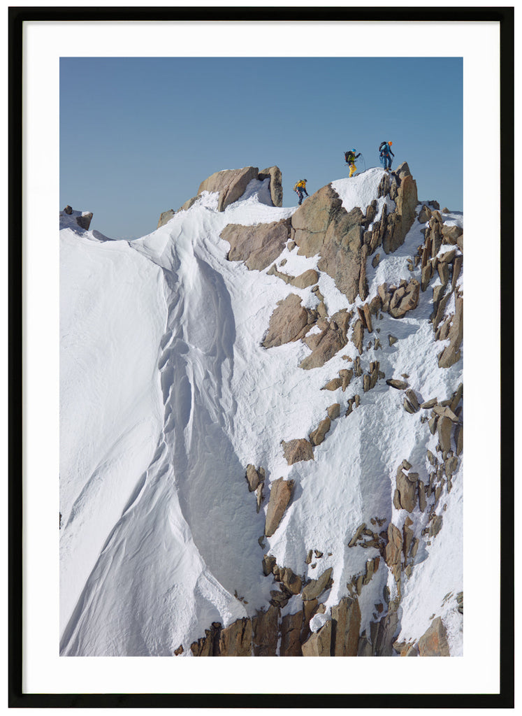 Color photograph of three mountain climbers on top of steep cliffs. Black frame.