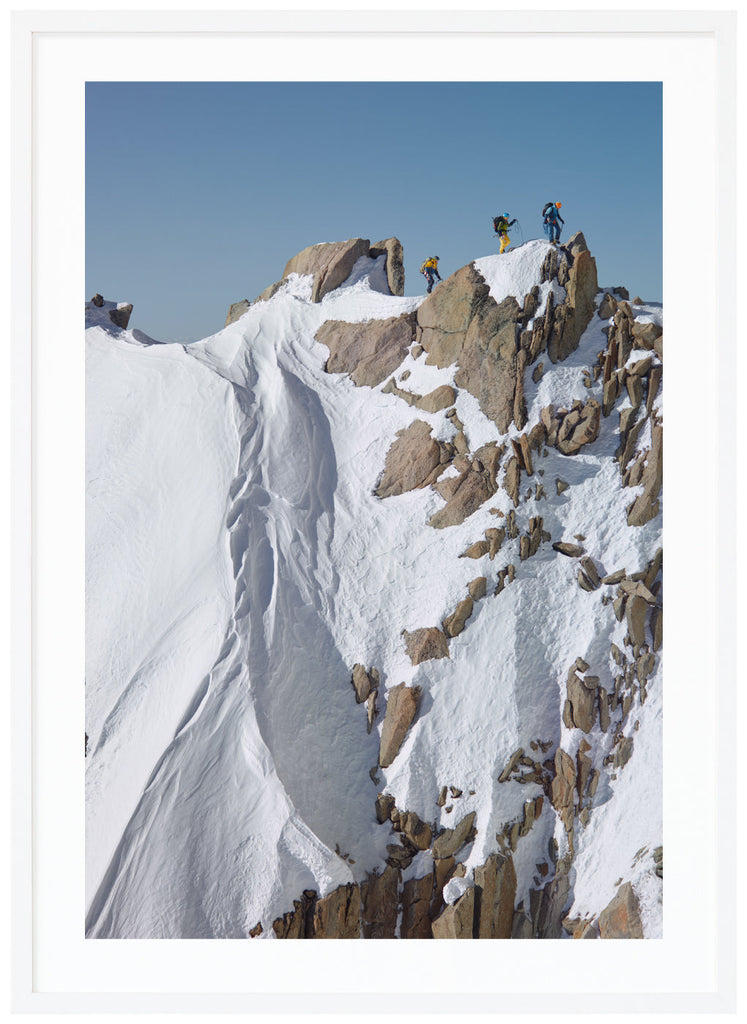 Color photograph of three mountain climbers on top of steep cliffs. White frame. 
