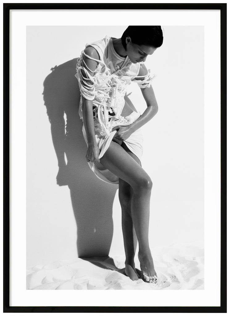 Black and white photograph a posing woman in white stringy clothes. Black frame. 