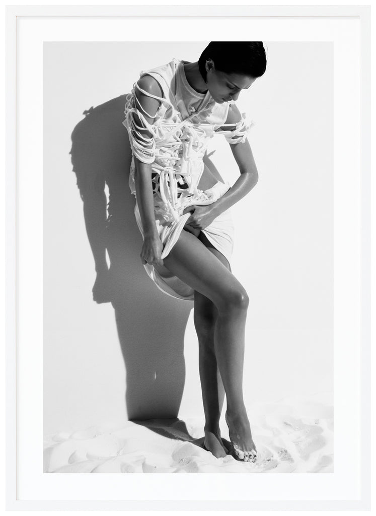 Black and white photograph a posing woman in white stringy clothes. White frame. 