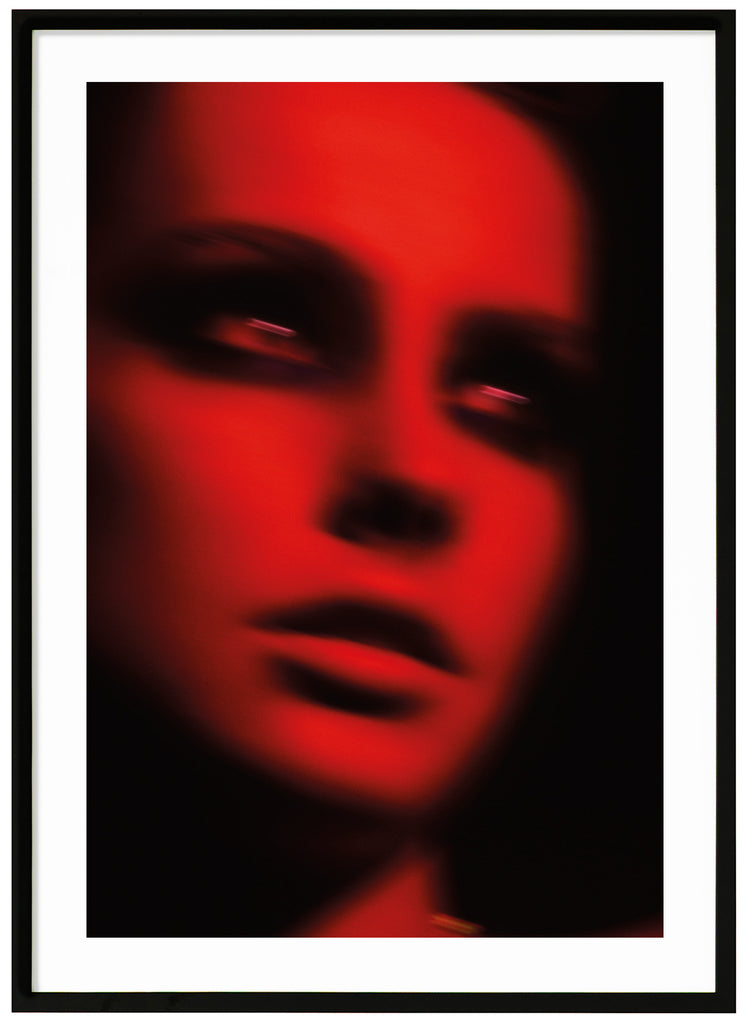 Photograph in the tones red and black, by a woman in black makeup around the eyes. Black frame. 