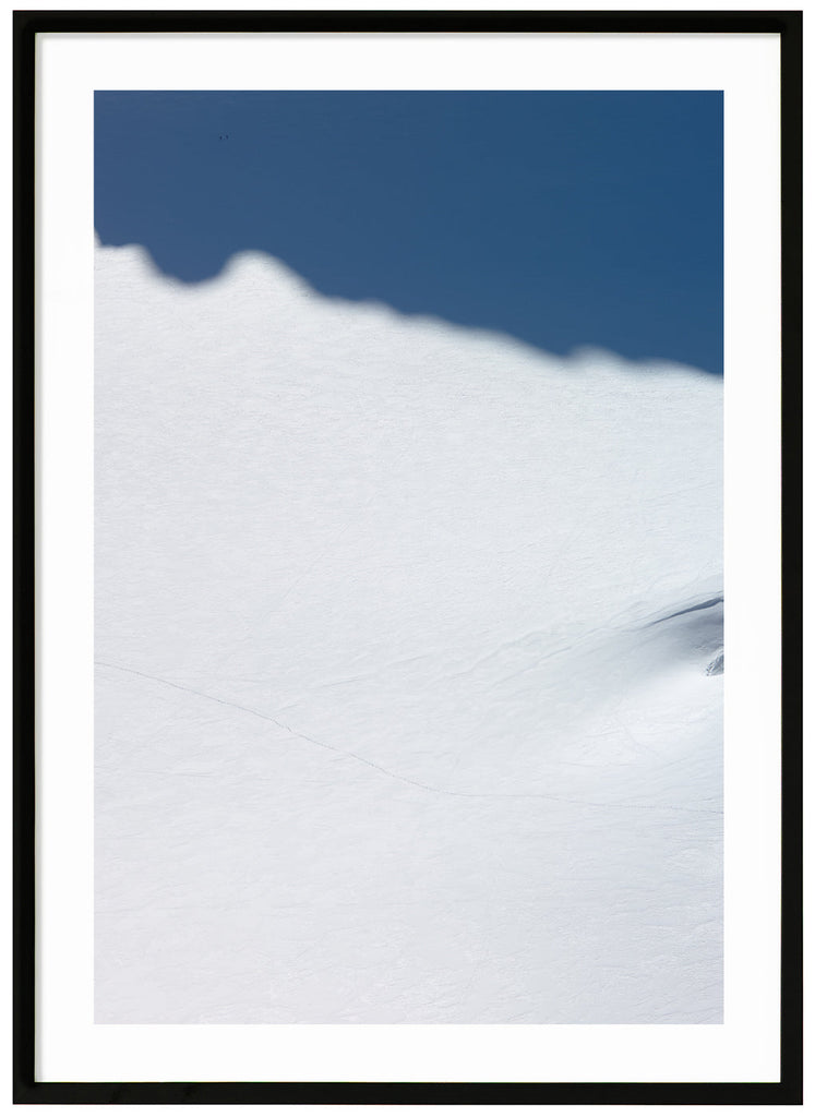 Color photography of a huge snow-covered surface with two skiers who are barely visible. Black frame.