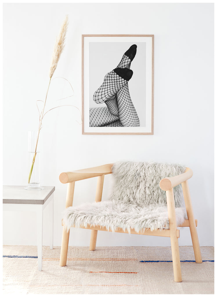 Black and white photograph of a woman's legs with her feet angled towards the camera, she is wearing net tights. Oak frame, wall.